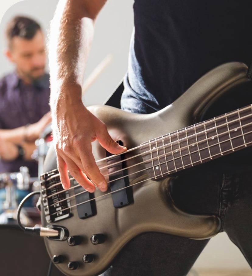 Guy playing a bass guitar with a guy playing drums in the background.
